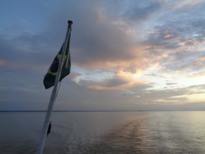 Das Foto ist vom Boot nach hinten aus aufgenommen. Man sieht eine Flagge und einen wunderschönen Himmel bei Sonnenaufgang.