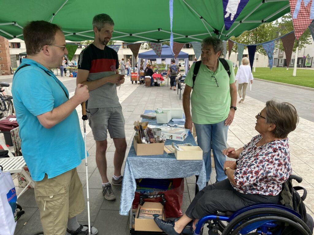 Beim Stand von Menschen in Hanau unterhalten sich die Aktiven. Zu sehen ist Marc-Eric mit seinem Blindenstock, Daniel, Peter und Marianne im Rollstuhl.