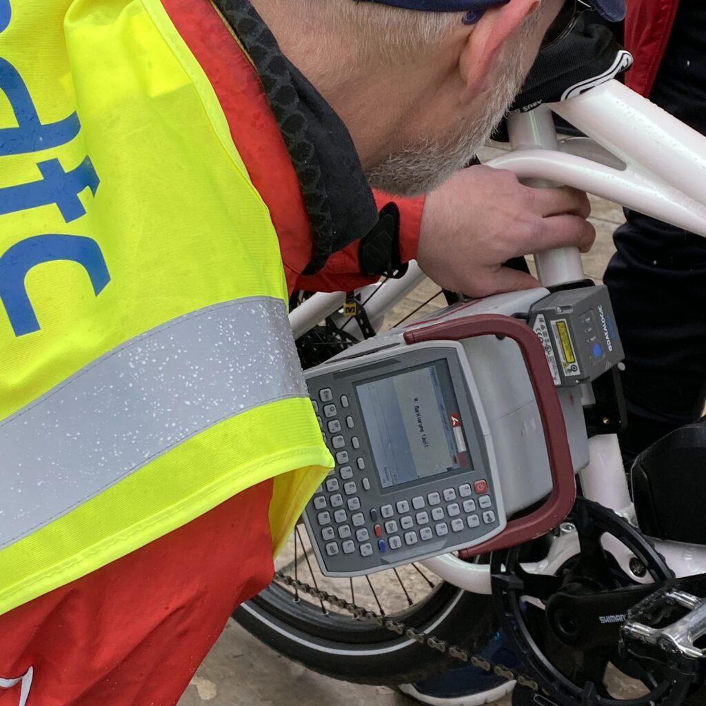 Zu sehen ist ein Detail eines Fahrrades. Ein Mann kniet davor und codiert mit einer kleinen Maschine eine Ziffernfolge auf die Radstange.