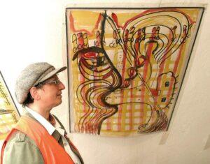 Felicitas Adler steht vor einem ihrer Kunstwerke, das an einer Wand hängt. 
