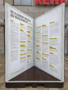 Das Bild zeigt ein überdimensional großes Buch, dass aufgeschlagen ist. Der Betrachter schaut auf die Innenseiten des Buches und kann die Allgemeine Erklärung der Menschenrechte lesen. 
