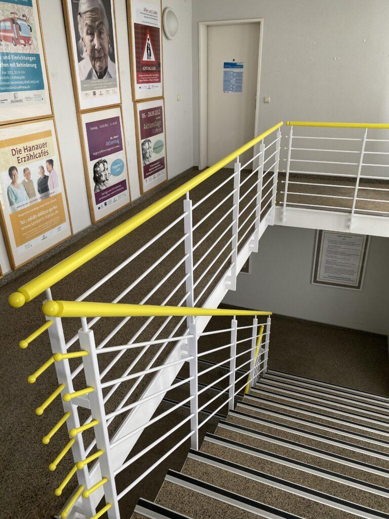 Treppenhaus mit einem Treppengeländer deren Handlauf in leuchtendem Gelb gestrichen ist.