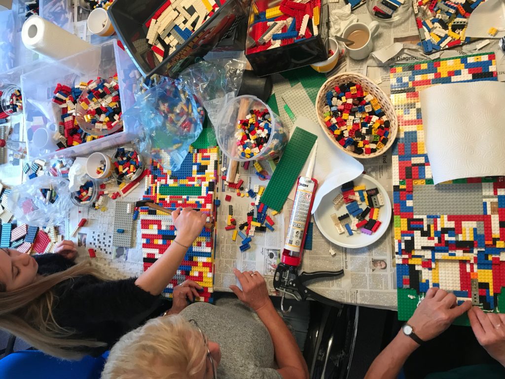 Vielfalt der Steine auf dem Tisch. Drei Damen sitzen vor einem Tisch, auf dem überall bunte LEGO-Steine verteilt sind.