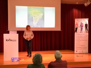 Elke beginnt ihren Vortrag mit einer Karte Südamerikas. Elke steht auf der Bühne, die Leinwand ist an und rechts steht der Menschen in Hanau Rollup.