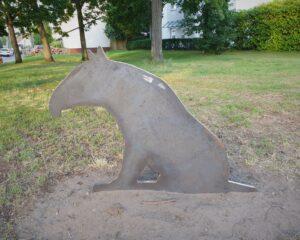 Ein 2-dimensionales Tapir aus Stahl sitzt auf einer Wiese.