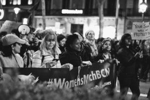 Auf diesem Bild sind mehrere Frauen zu sehen, die für ihre Rechte demonstrieren. Sie gehen auf die Straßen und wollen auf sich aufmerksam machen. Rechts hält eine Frau ein Schild hoch auf dem steht:"Euer Schweigen schützt Euch nicht". 