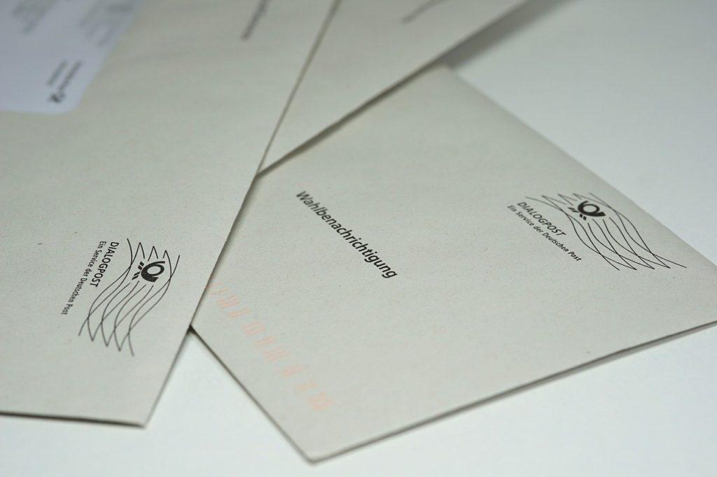 In dem Bild sind drei graue Briefumschläge übereinandergelegt mit dem Wort Wahlbenachrichtigung zu sehen.