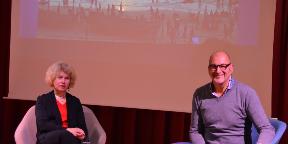 Das Bild zeigt Silvia Schäfer und den Moderator auf der Bühne sitzend und dahinter ein Bild einer der Reisen.