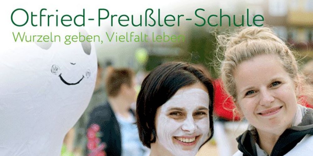 Ein Bild der Startseite von der Ottfried-Preußler-Schule in Hannover. Zwei Frauen sind im Vordergrund zu sehen, hinten viele andere Menschen. Beide lächeln, die eine Dame hat ihr Gesicht weiß angemalt.