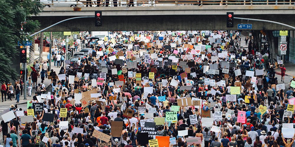 Eine Menschenmenge protestiert. Das Bild ist gefüllt mit Menschen, die Schilder hochalten, mit verschiednen Botschaften.