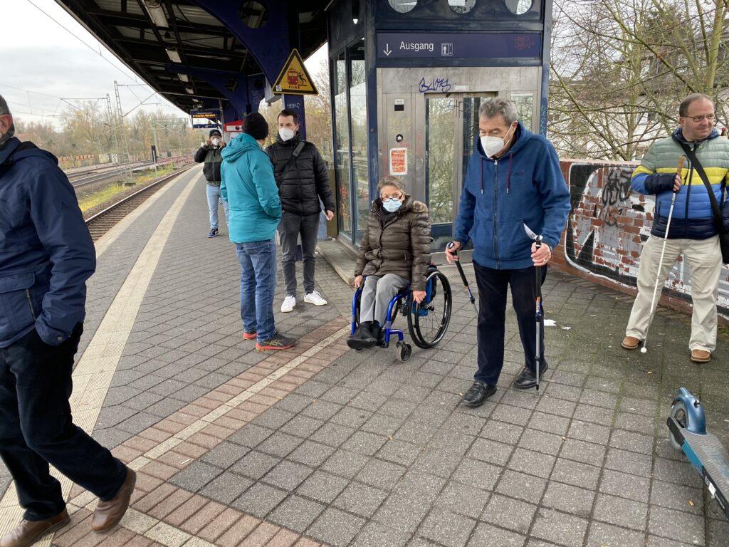 Eine Personengruppe steht auf dem Bahnsteig in Hanau Steinheim und begutachtet die Situatiob um den Aufzug und die Leitstreifen