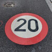 Ein großes, rot-weisses Tempo 20 Gebotszeichen ist auf eine Asphaltstraße gesprüht.