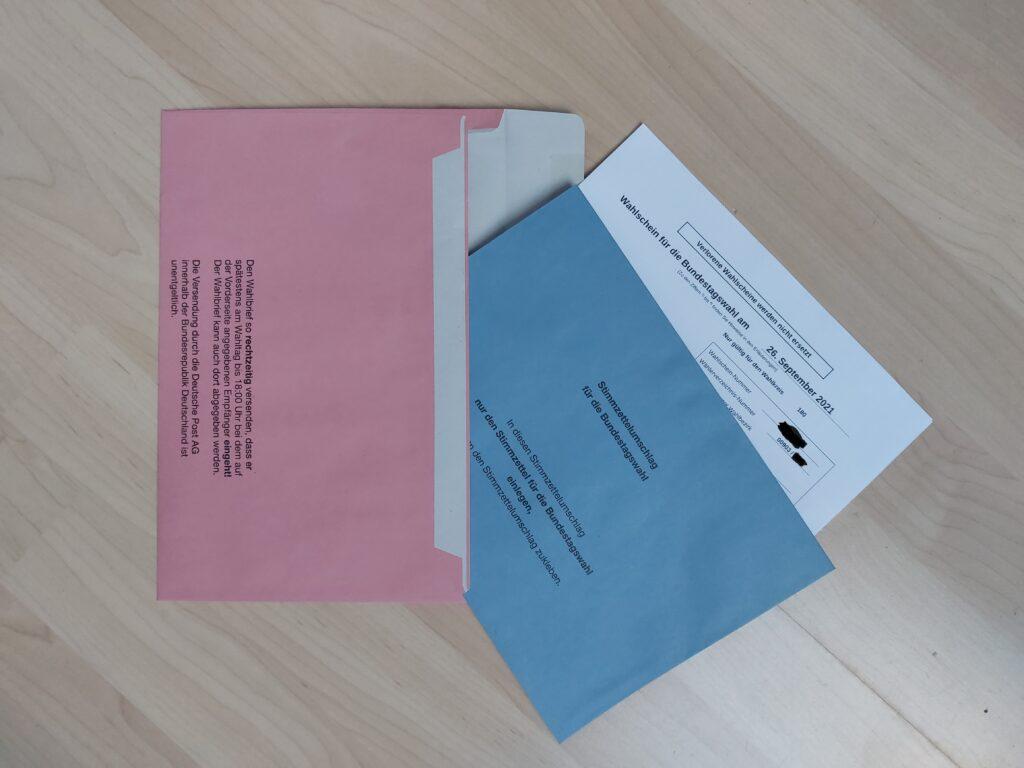 Zu sehen ist der blaue, zugeklebte Umschlag mit dem Stimmzettel, der zusammen mit dem Wahlschein in den roten Briefumschlag gesteckt wird.